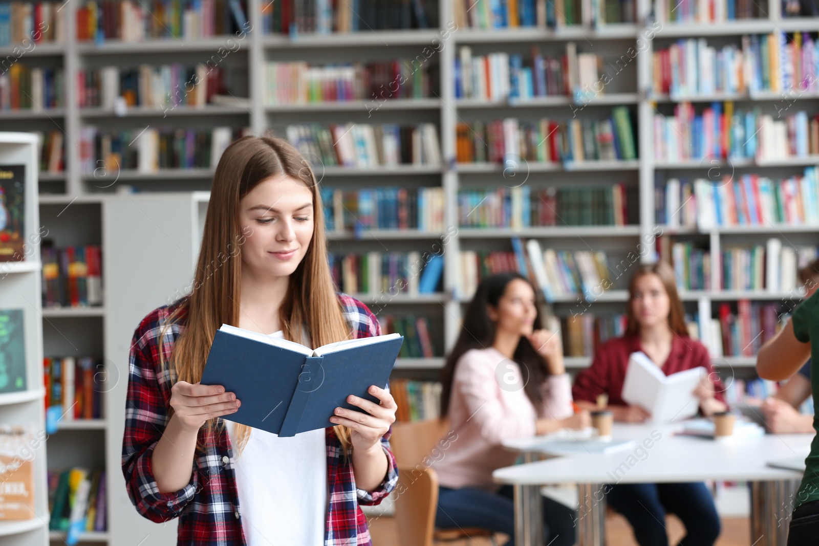 Photo of Young pretty woman reading book in library. Space for text