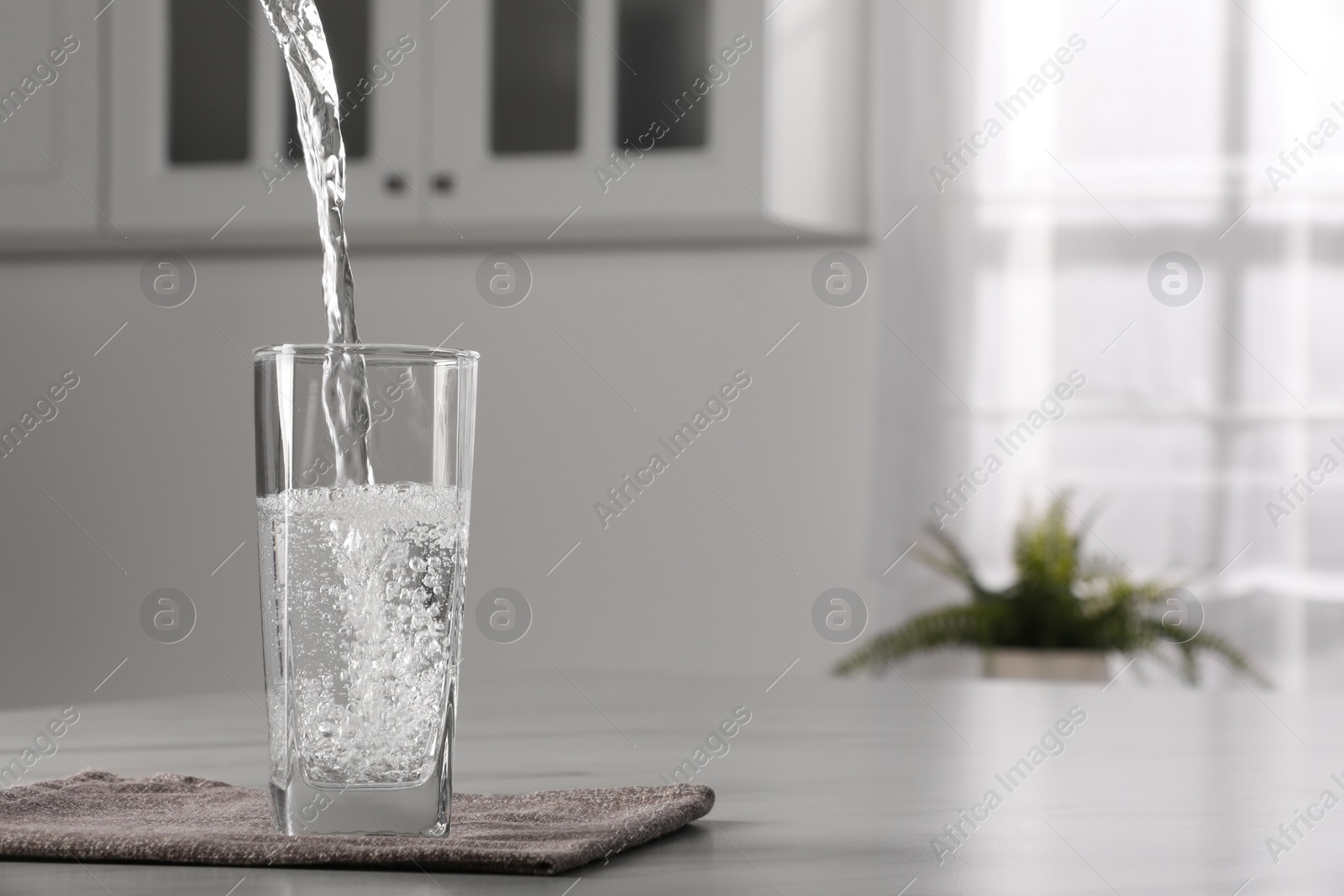 Photo of Pouring water into glass at table indoors, space for text