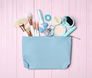 Cosmetic bag with makeup products and beauty accessories on pink wooden background, flat lay