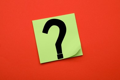 Sticky note with question mark on dark orange background, top view