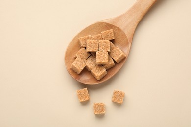 Photo of Brown sugar cubes in wooden spoon on beige background, top view