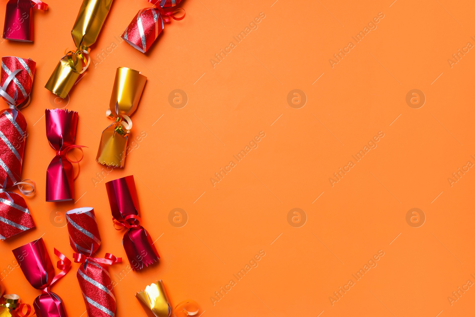 Photo of Different Christmas crackers on orange background, flat lay. Space for text