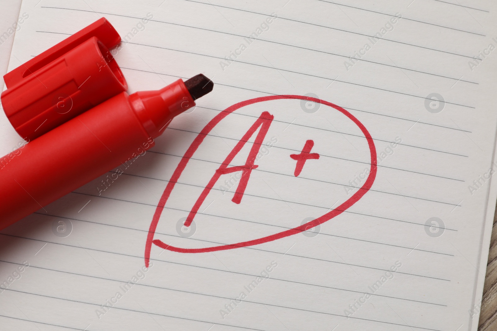 Photo of School grade. Red letter A with plus symbol on notebook paper and marker, top view