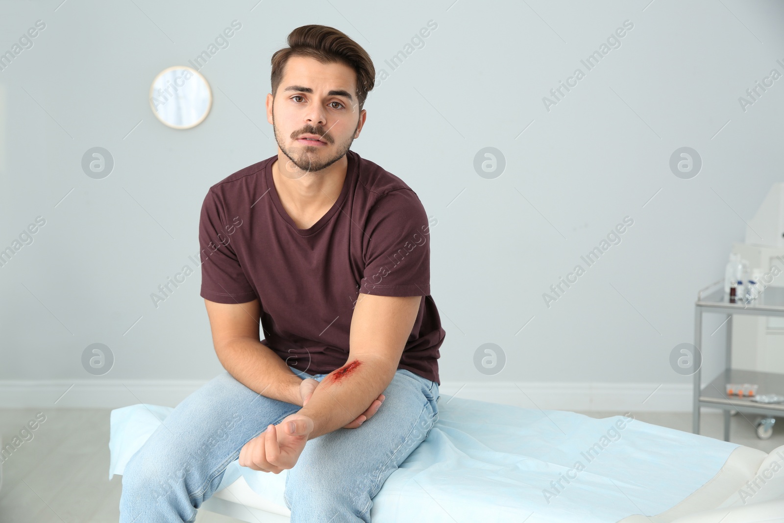 Photo of Young man with injured arm in clinic, space for text. First aid