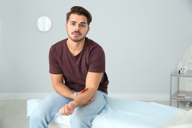 Photo of Young man with injured arm in clinic, space for text. First aid