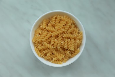 Photo of Bowl with uncooked fusilli pasta on white marble table, top view