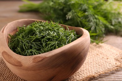 Photo of Fresh cut dill in bowl on wooden table, closeup