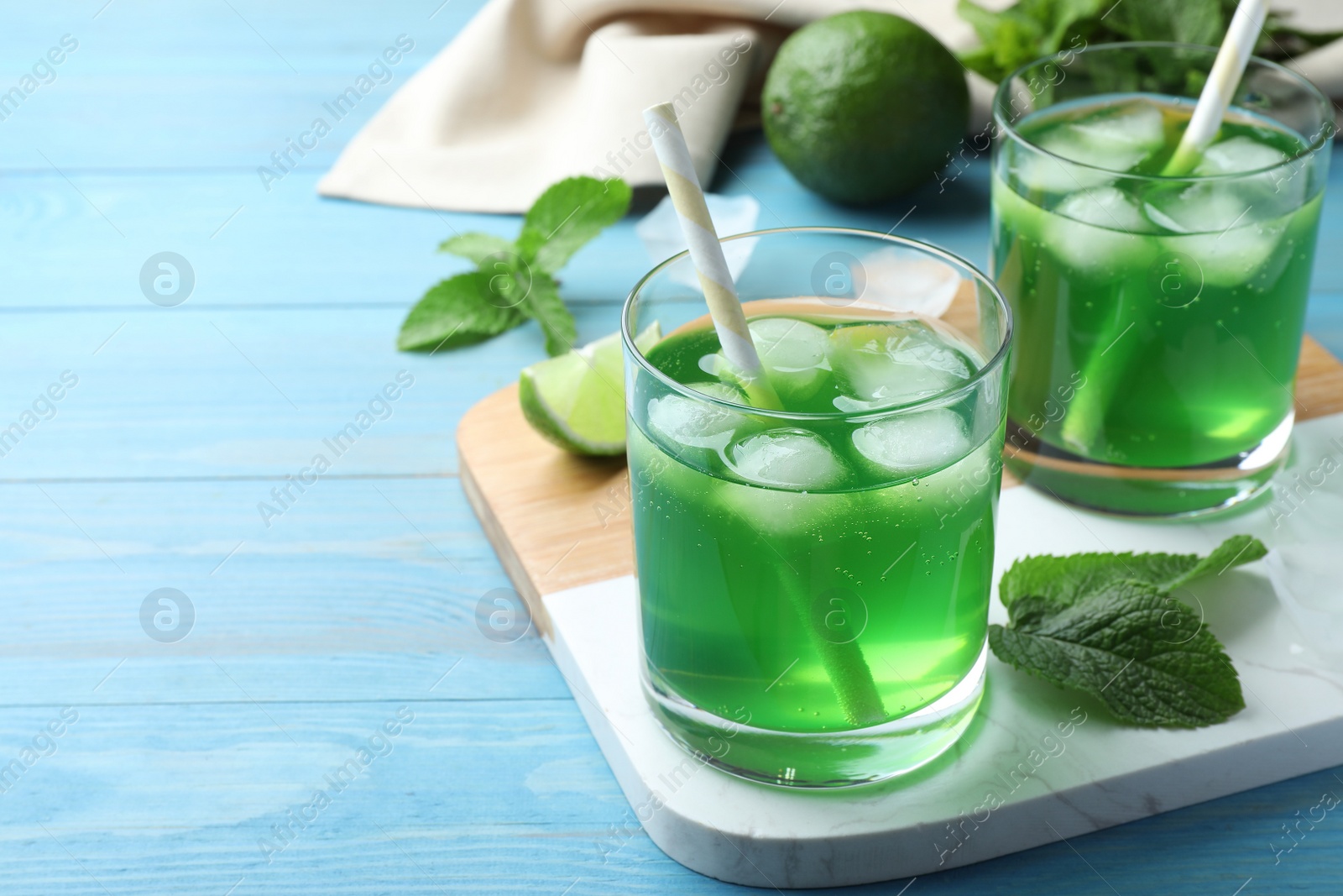 Photo of Delicious mint liqueur with green leaves and ice cubes on turquoise wooden table. Space for text