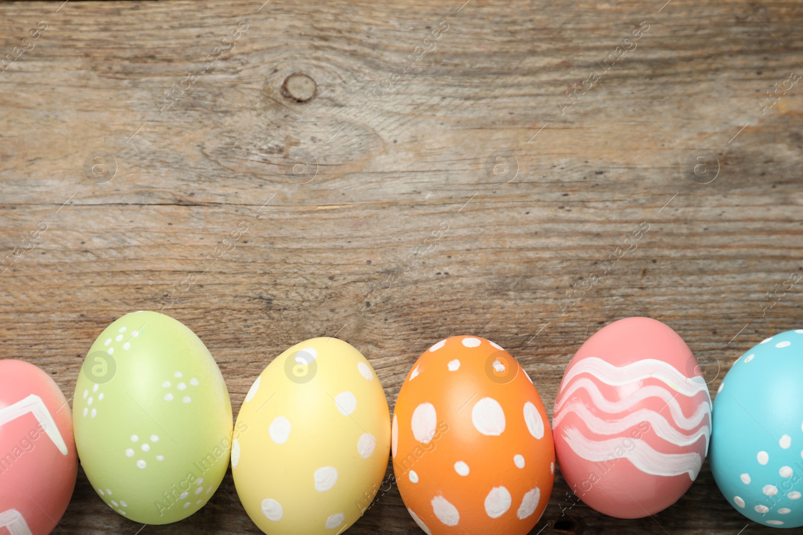 Photo of Flat lay composition of painted Easter eggs on wooden background, space for text