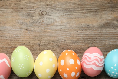 Flat lay composition of painted Easter eggs on wooden background, space for text