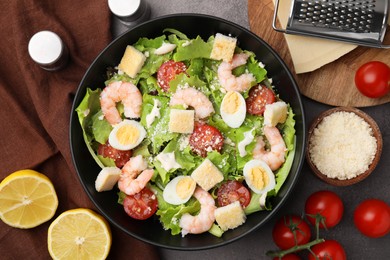 Photo of Delicious Caesar salad with shrimps and ingredients on brown table, flat lay