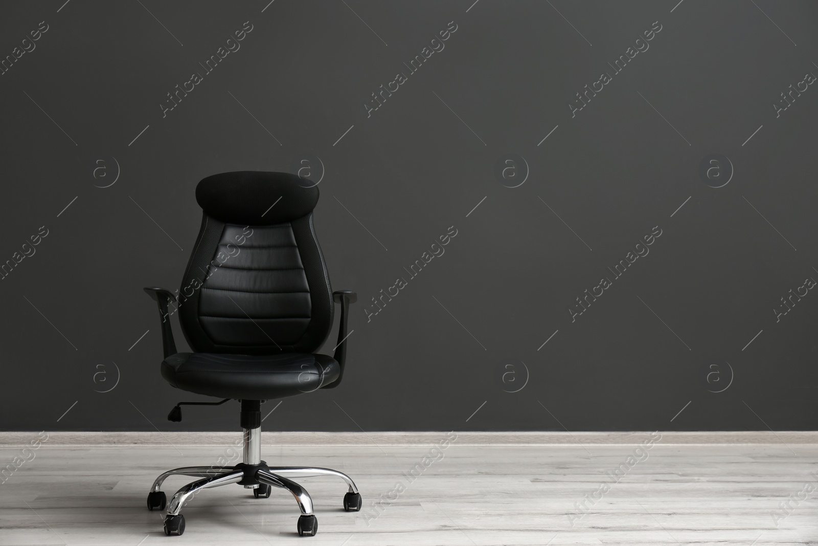 Photo of Comfortable office chair near black wall indoors. Space for text