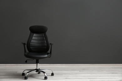 Comfortable office chair near black wall indoors. Space for text