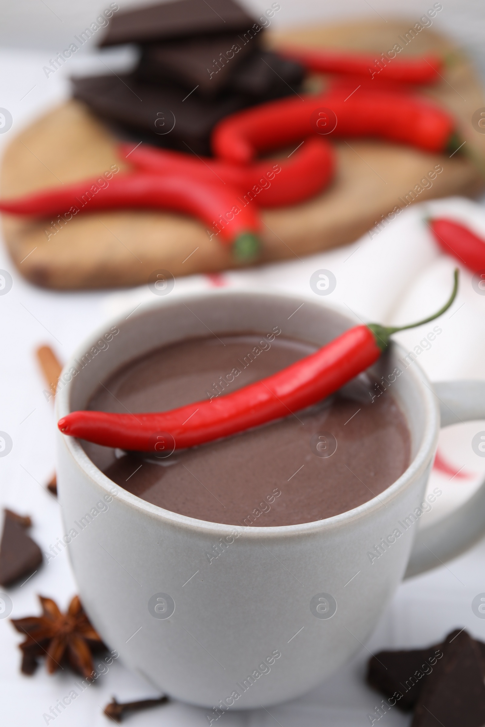 Photo of Cup of hot chocolate with chili pepper on white tiled table, closeup