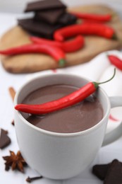 Photo of Cup of hot chocolate with chili pepper on white tiled table, closeup