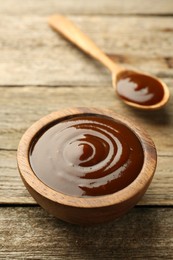 Photo of Tasty barbeque sauce in bowl and spoon on wooden table