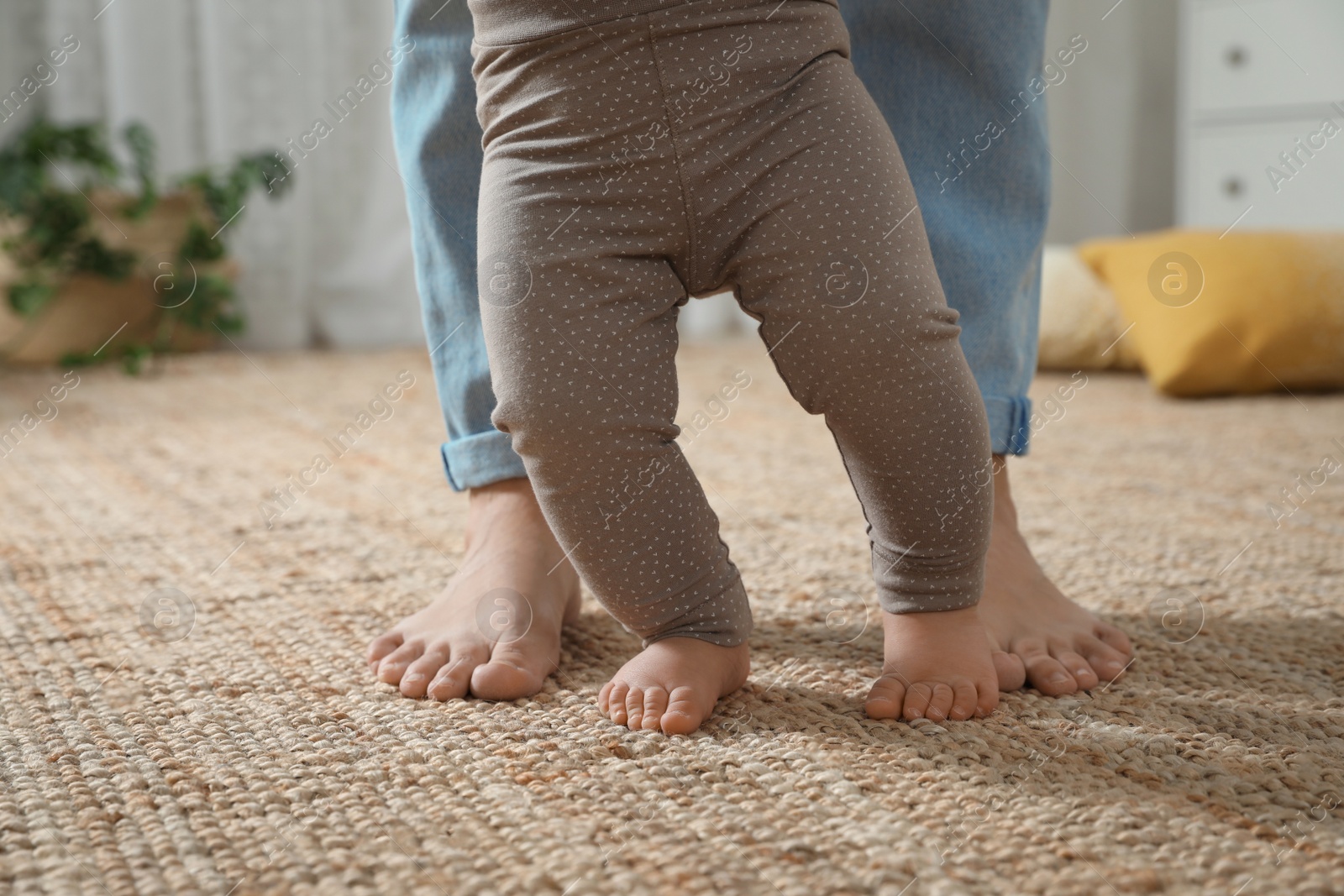 Photo of Mother supporting her baby daughter while she learning to walk at home, closeup