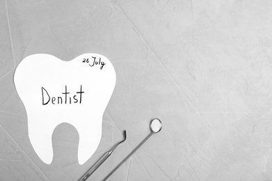 Photo of Paper tooth cutout and dentist tools on grey background, flat lay. Space for text