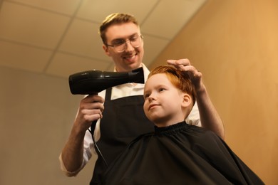 Professional hairdresser drying boy's hair in beauty salon, low angle view