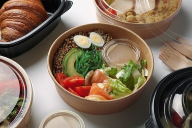 Photo of Tasty food in containers with wooden knives and forks on light grey table