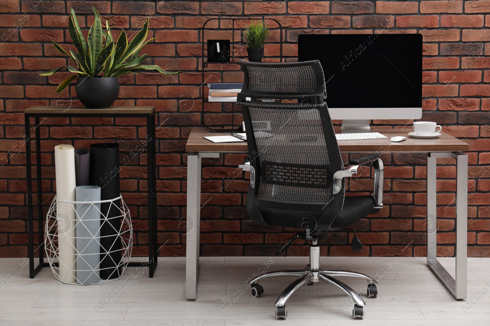 Photo of Cosy workspace with computer on desk, chair and potted plants near brick wall at home