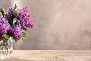 Photo of Beautiful lilac flowers in vase on wooden table, space for text