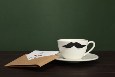 Photo of Happy Father's Day. Card with phrase I Love You, Daddy in envelope and cup of coffee on wooden table, closeup