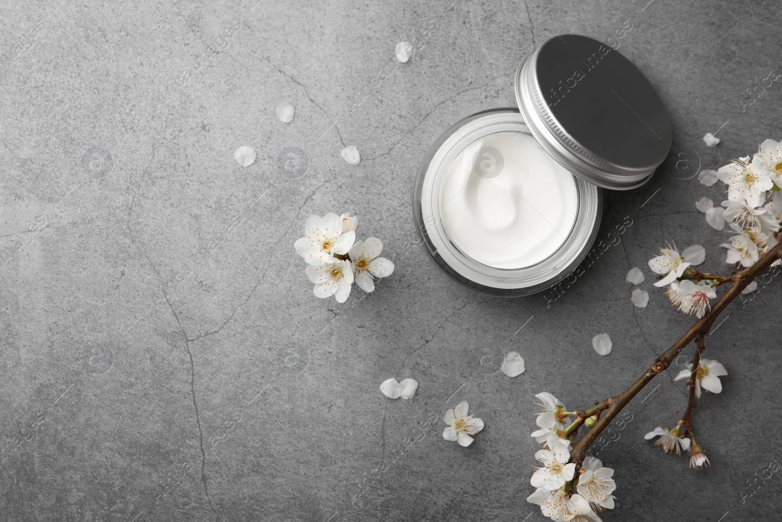 Photo of Flat lay composition with jar of face cream and flowers on grey table. Space for text