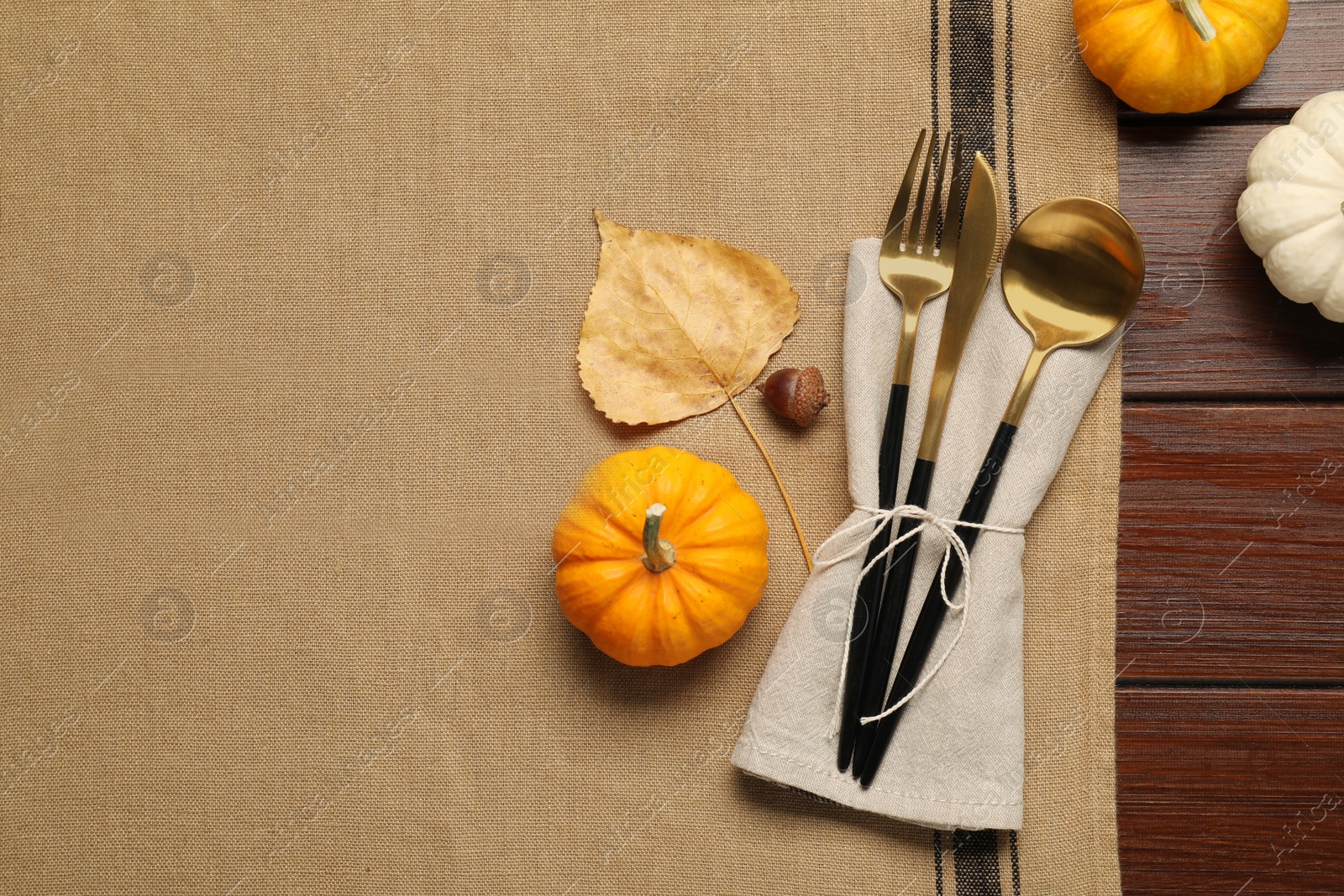 Photo of Cutlery, napkin and pumpkins on brown tablecloth, flat lay with space for text. Table setting