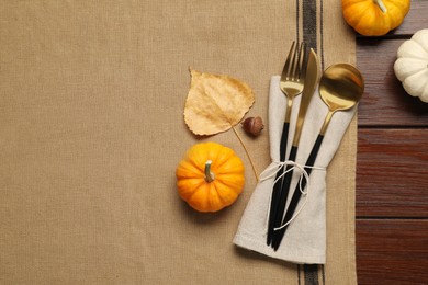 Photo of Cutlery, napkin and pumpkins on brown tablecloth, flat lay with space for text. Table setting