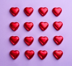 Photo of Heart shaped chocolate candies in red foil on violet background, flat lay