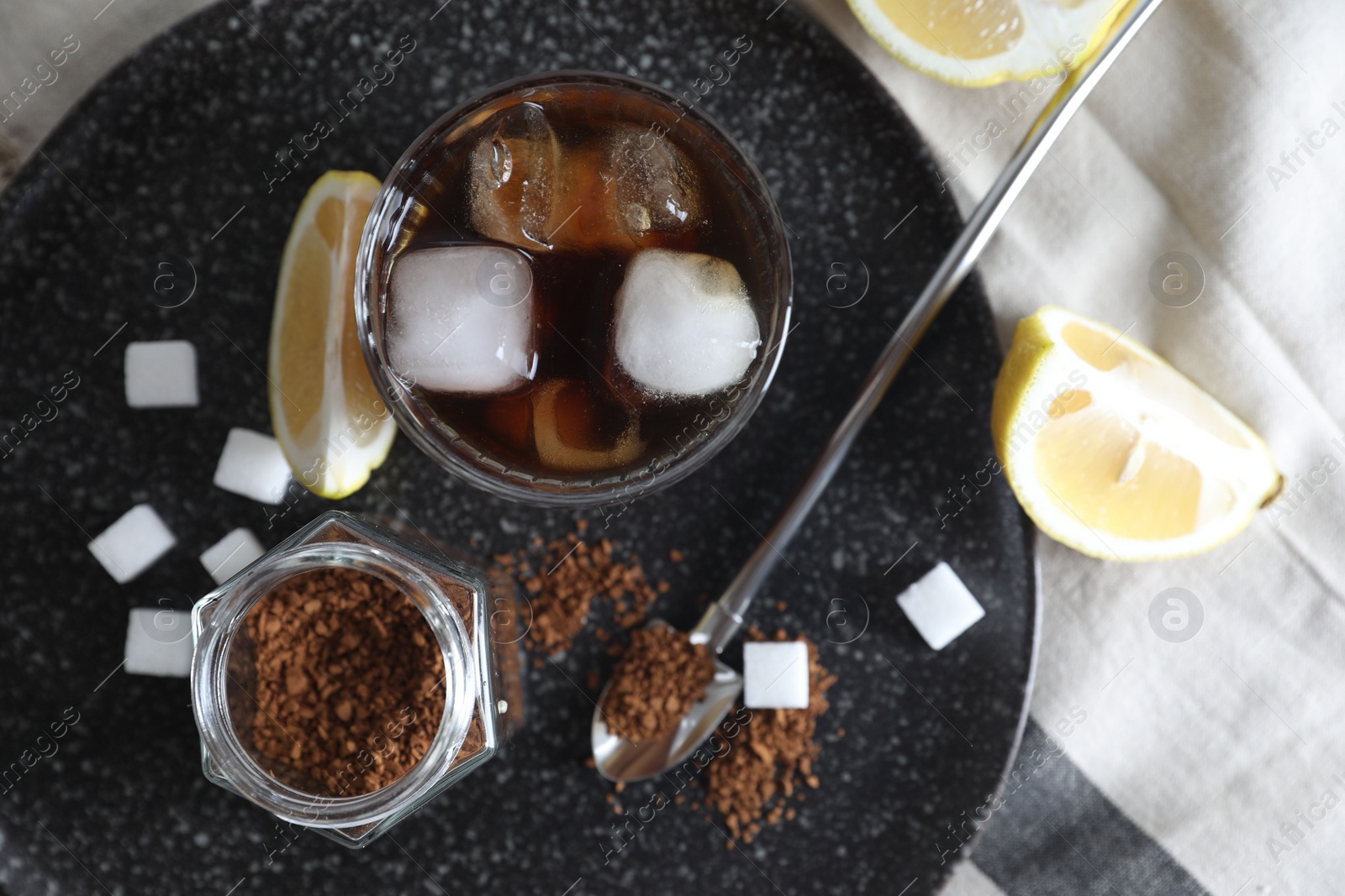 Photo of Refreshing iced coffee in glass, sugar cubes, lemon and spoon on cloth, top view