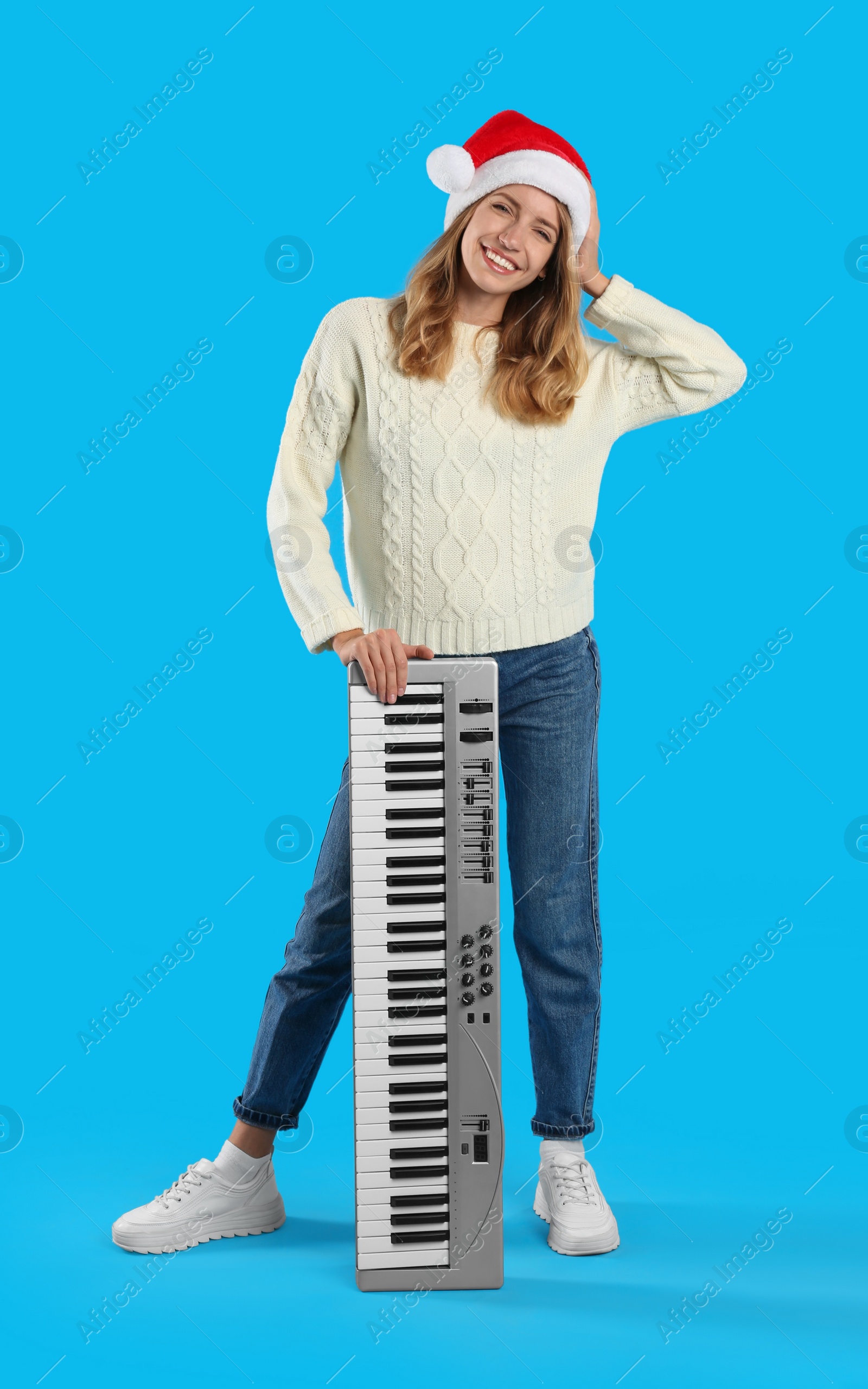 Photo of Young woman in Santa hat with synthesizer on light blue background. Christmas music