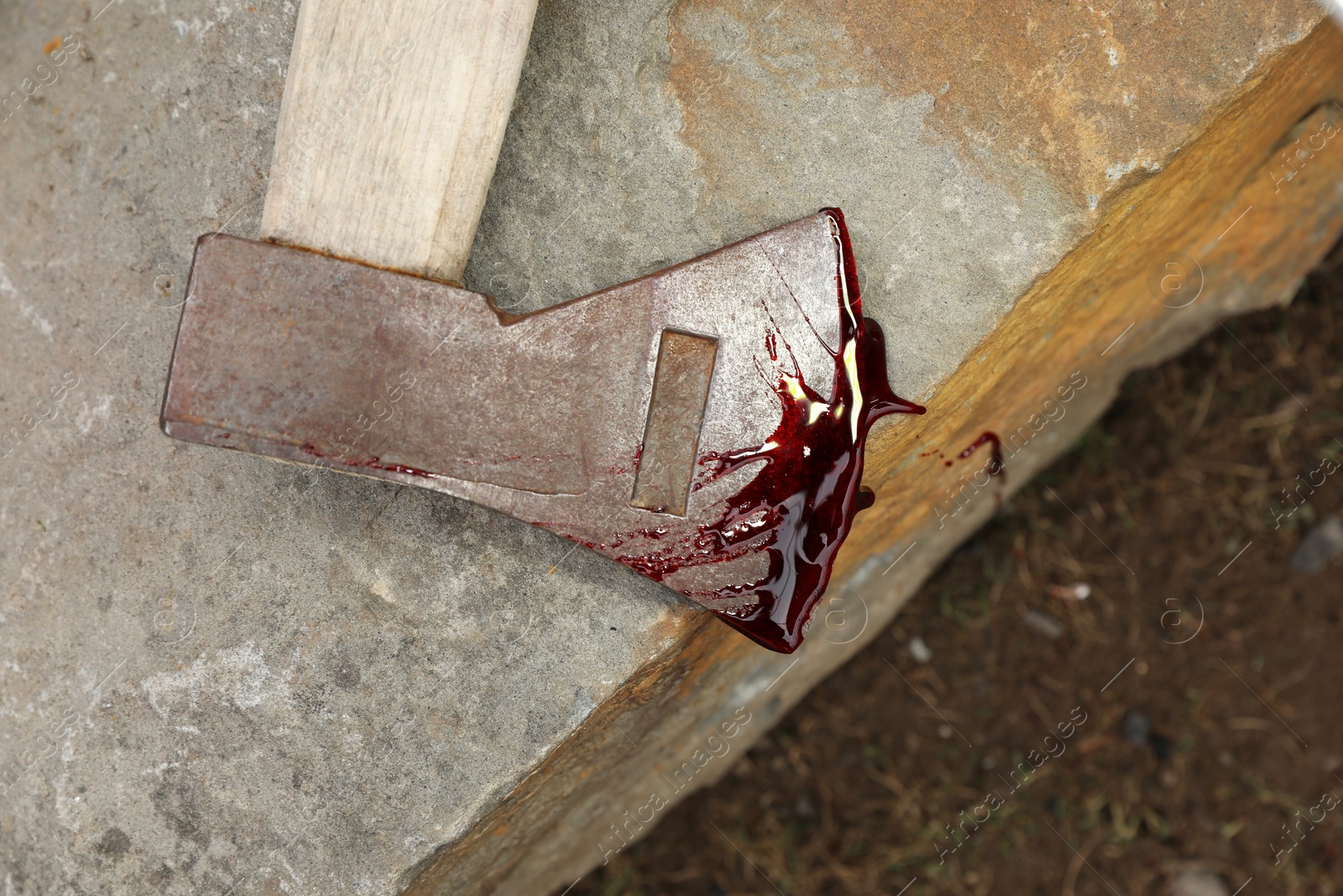 Photo of Axe with blood on stone outdoors, top view