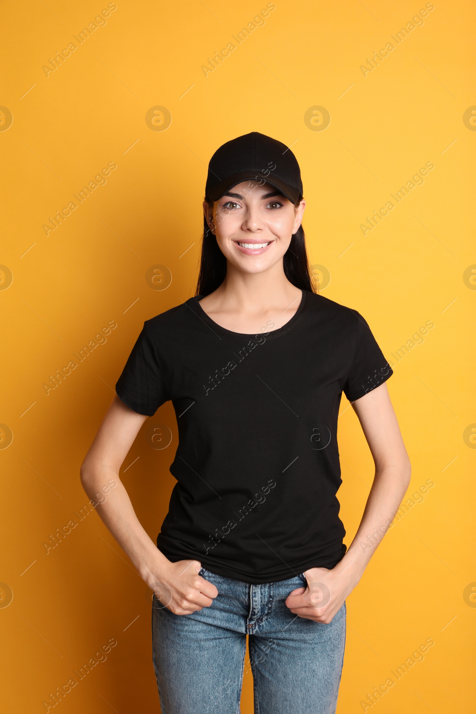 Photo of Young happy woman in black cap and tshirt on yellow background. Mockup for design