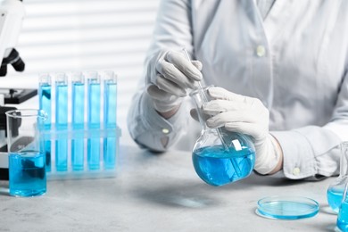 Photo of Scientist taking sample of light blue liquid at white table in laboratory, closeup