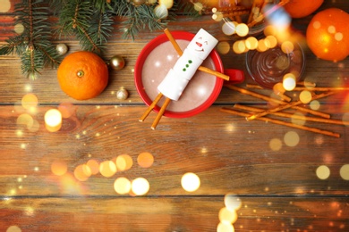 Image of Flat lay composition with marshmallow snowman in cup of hot drink on wooden table, space for text. Bokeh effect 