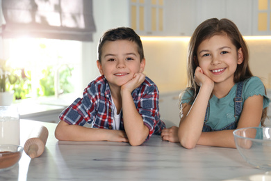 Cute little children at table with cooking ingredients in kitchen