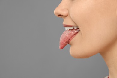 Photo of Happy young woman showing her tongue on grey background, closeup. Space for text