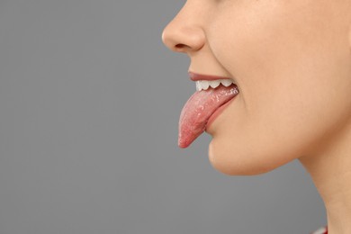 Happy young woman showing her tongue on grey background, closeup. Space for text