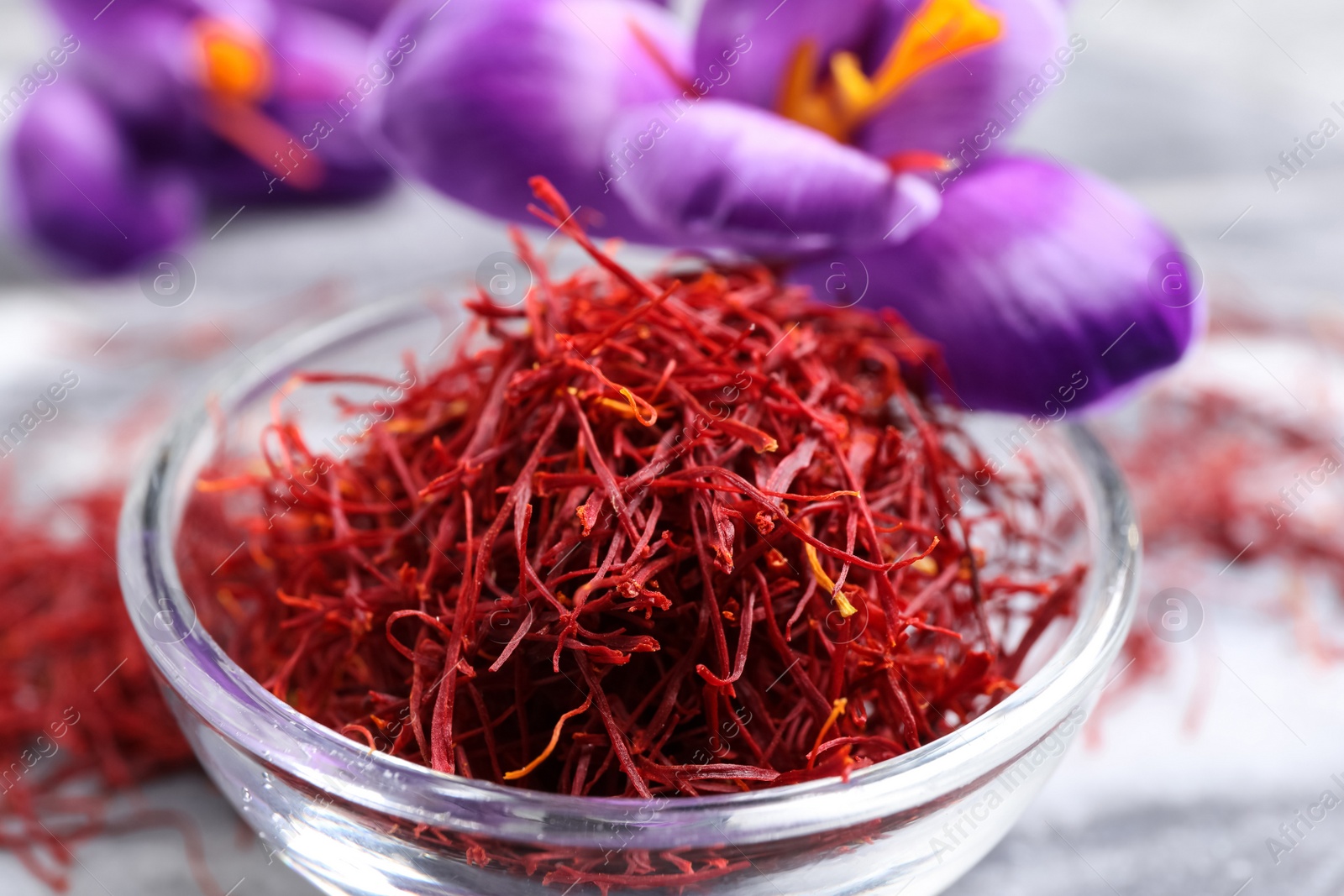 Photo of Dried saffron in bowl and crocus flowers on grey board, closeup