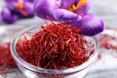 Dried saffron in bowl and crocus flowers on grey board, closeup