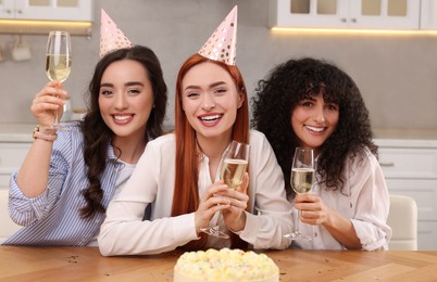 Photo of Happy young women with tasty cake and glassessparkling wine celebrating birthday in kitchen