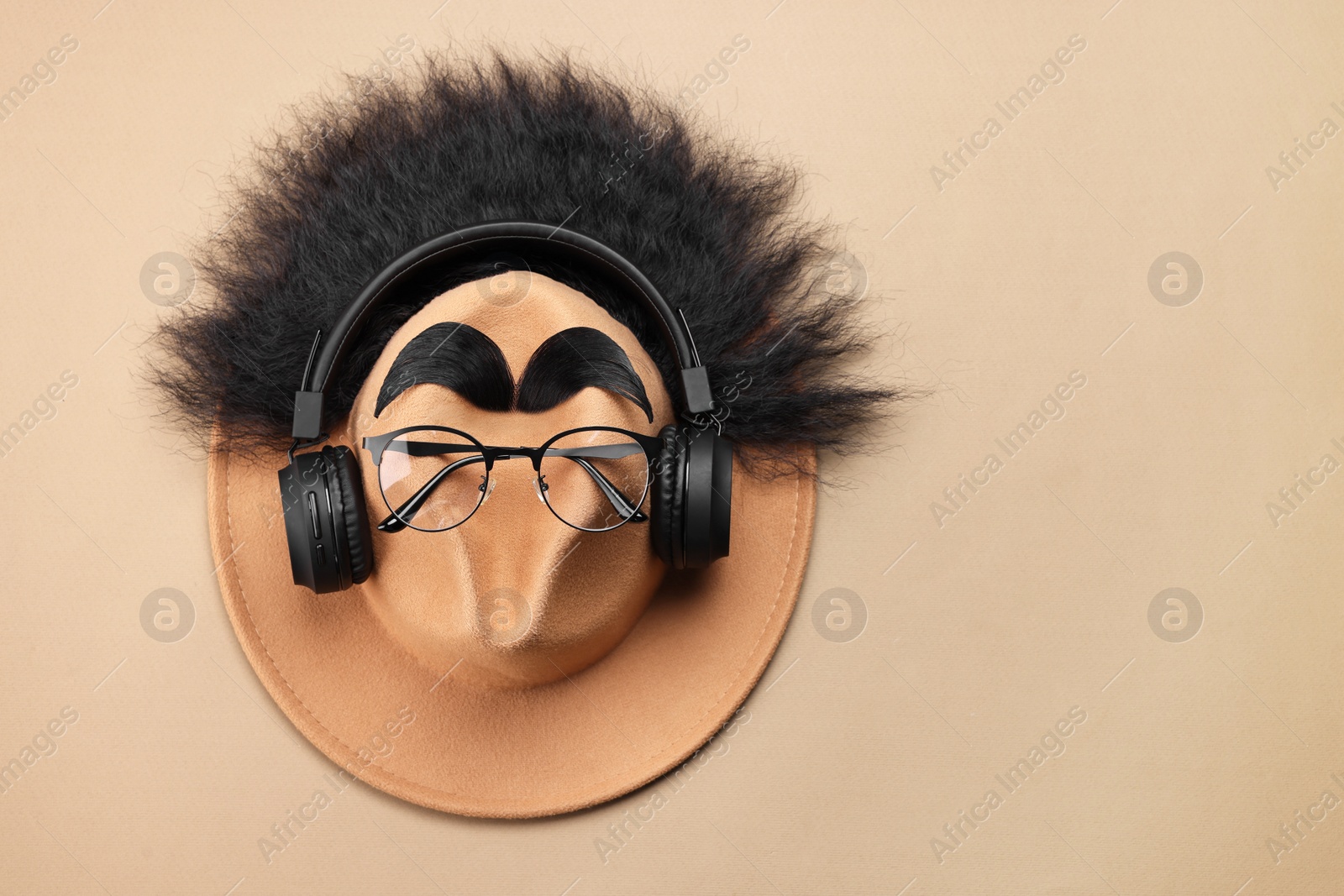 Photo of Man's face made of artificial hair, eyebrows, glasses and hat on beige background, top view. Space for text