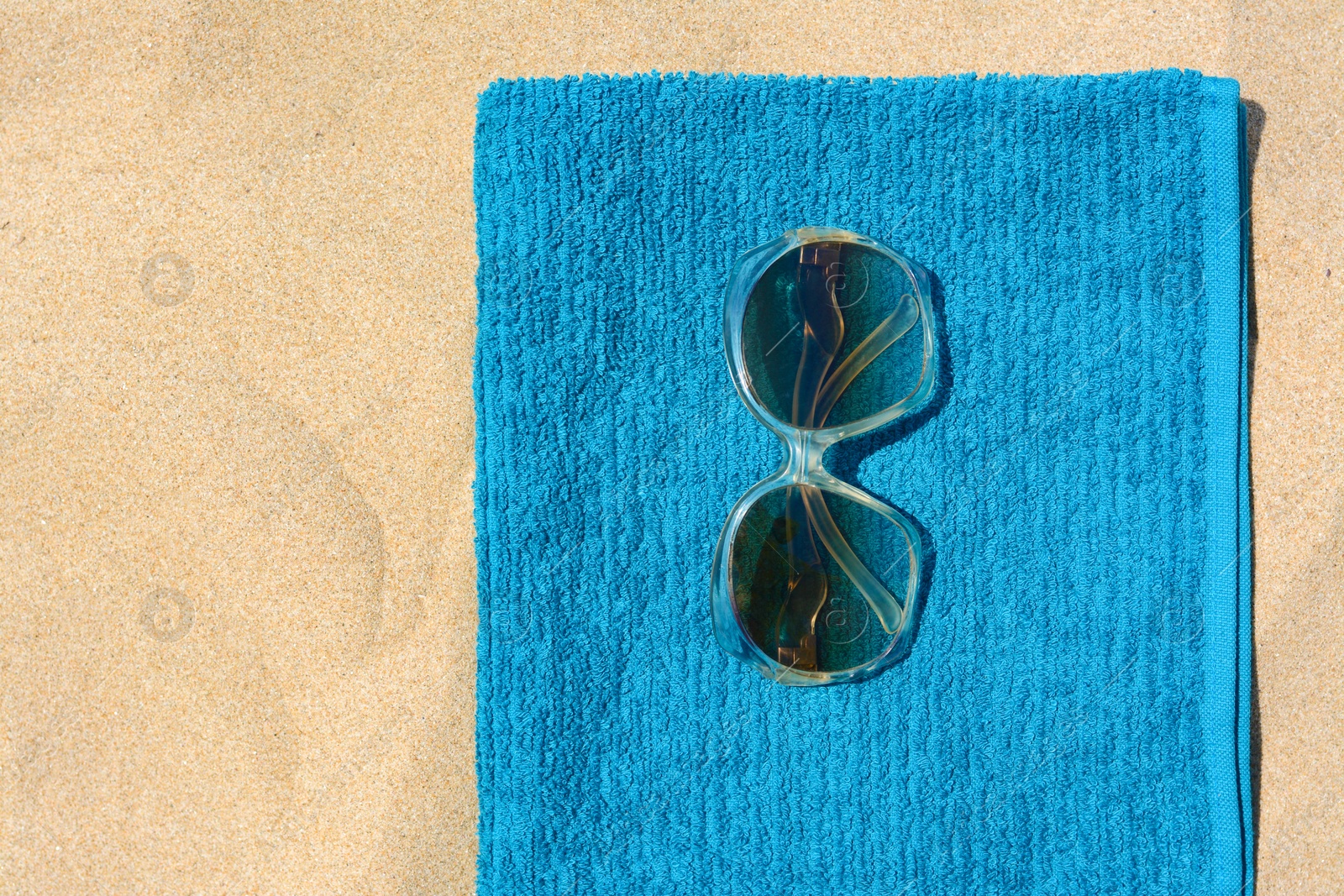 Photo of Soft blue beach towel with sunglasses on sand, top view. Space for text