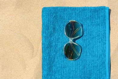 Soft blue beach towel with sunglasses on sand, top view. Space for text