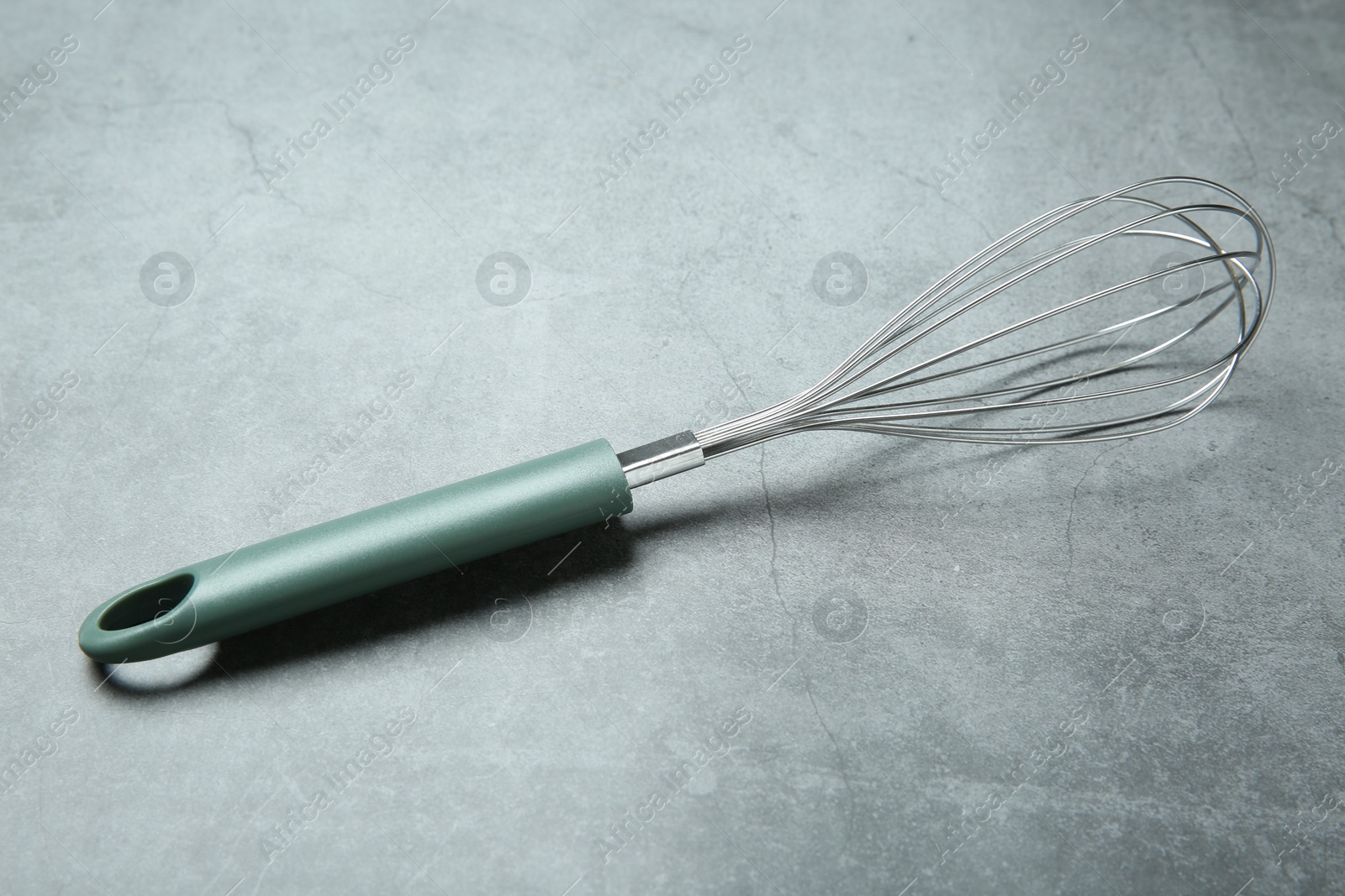 Photo of Metal whisk on gray table. Kitchen tool