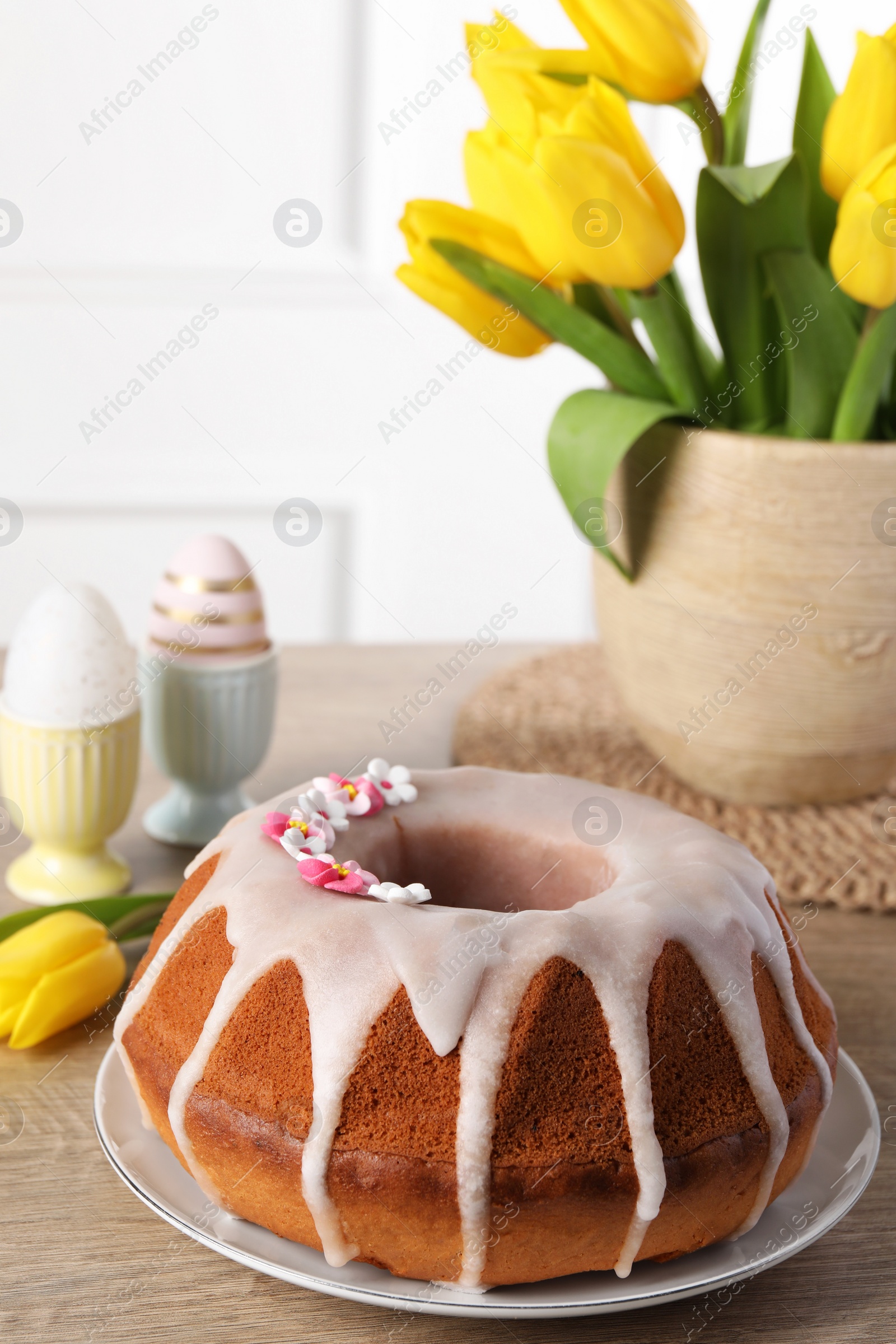 Photo of Delicious Easter cake decorated with sprinkles near beautiful tulips and painted eggs on wooden table