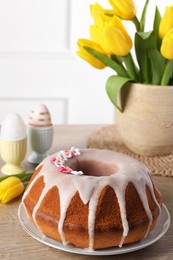 Delicious Easter cake decorated with sprinkles near beautiful tulips and painted eggs on wooden table
