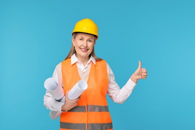 Photo of Architect in hard hat with drafts showing thumbs up on light blue background
